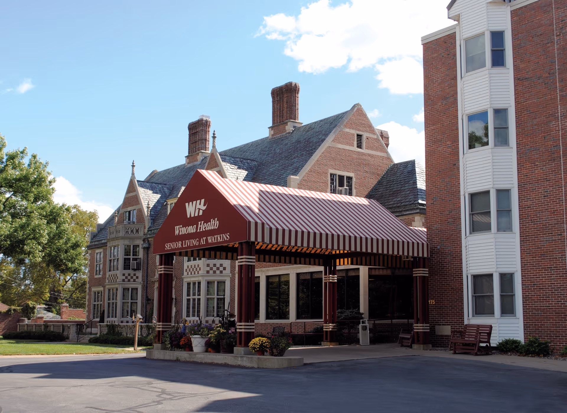 Front entrance of a brick senior living facility with a red-and-white striped canopy reading "Winona Health Senior Living at Watkins."