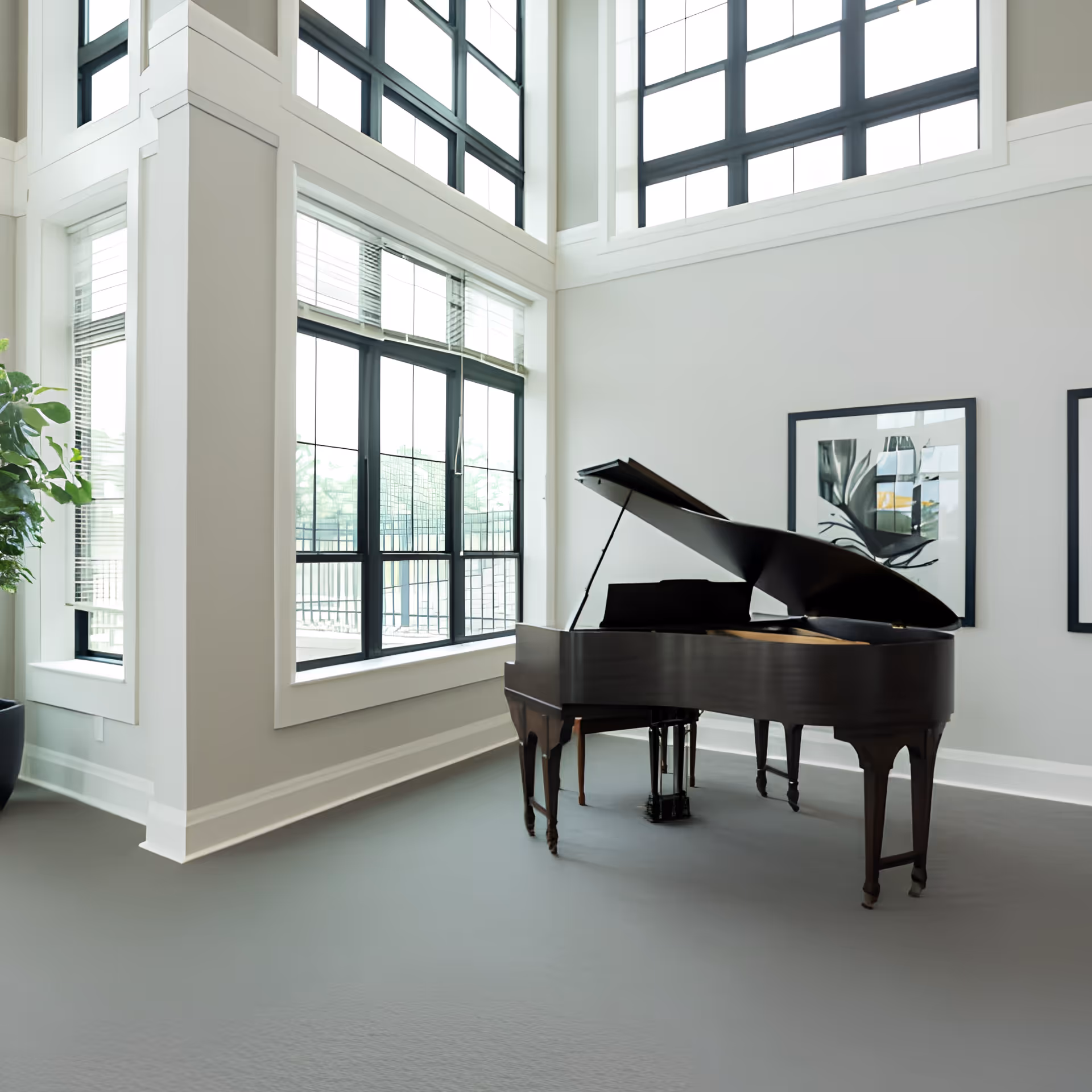 A bright, high‑ceilinged interior room with a grand piano near large windows and framed artwork on the wall.