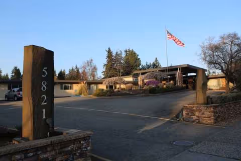 Entrance to a single-story senior living facility with stone pillars and an American flag.