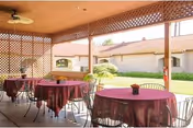 Covered outdoor patio with round tables draped in purple tablecloths, metal chairs, lattice privacy screens, and a landscaped courtyard with buildings beyond.