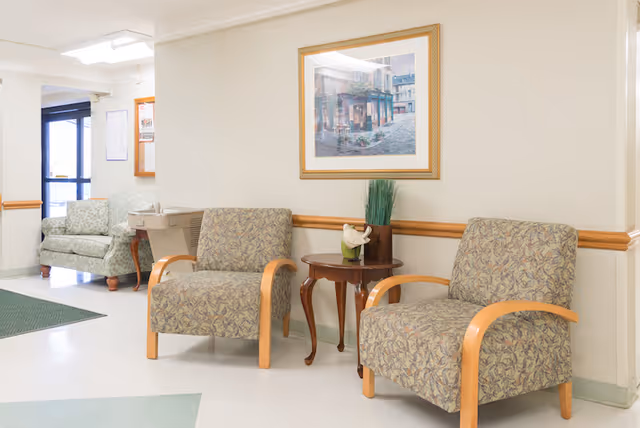 Small waiting area with upholstered chairs, a side table holding a plant, and a framed picture on the wall.