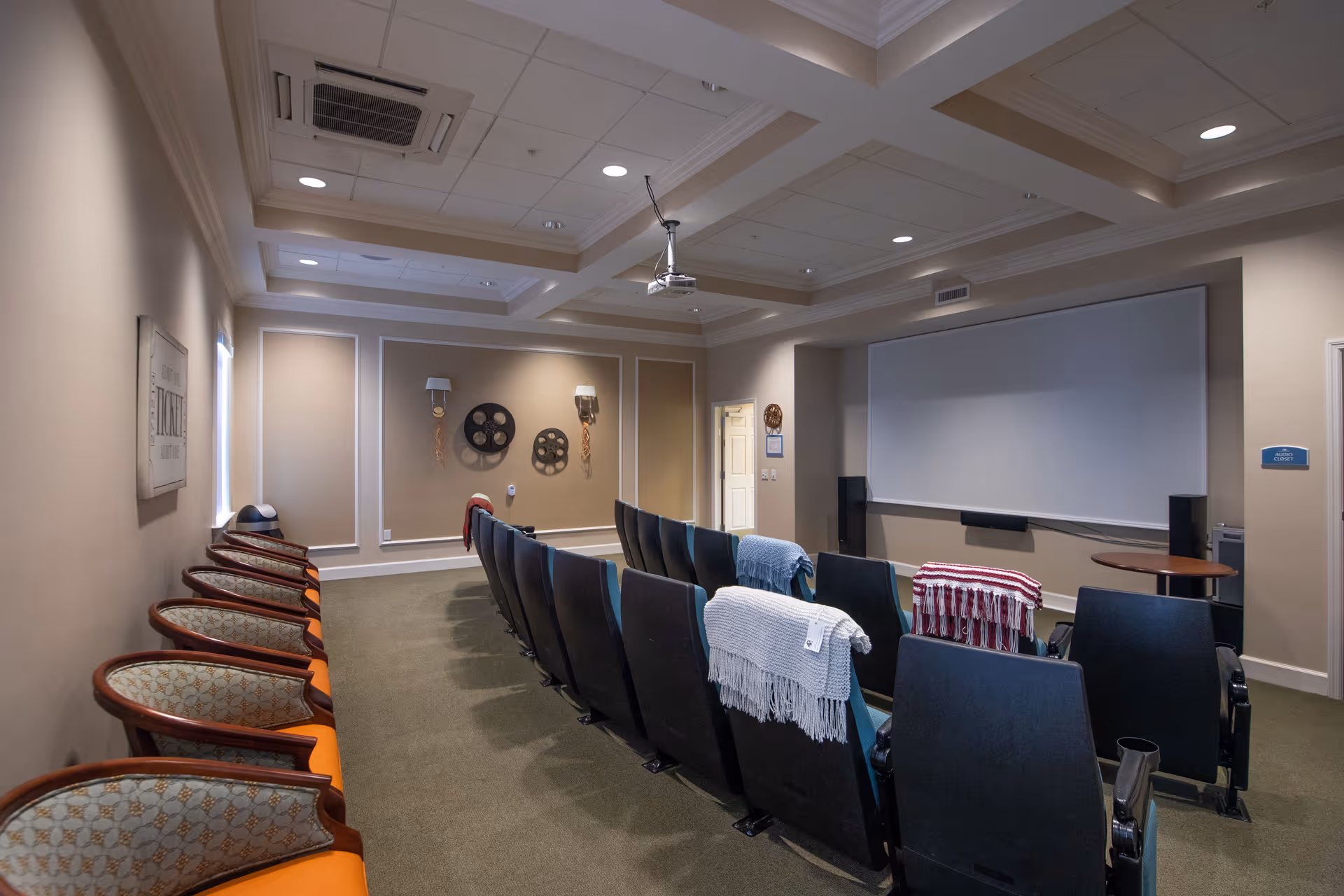 A small screening room with rows of theater seats facing a large projector screen and additional chairs along the side wall.