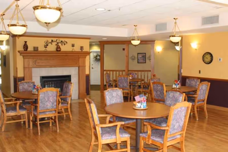 Community dining room with round wooden tables and upholstered chairs, a fireplace mantle, and pendant lights.