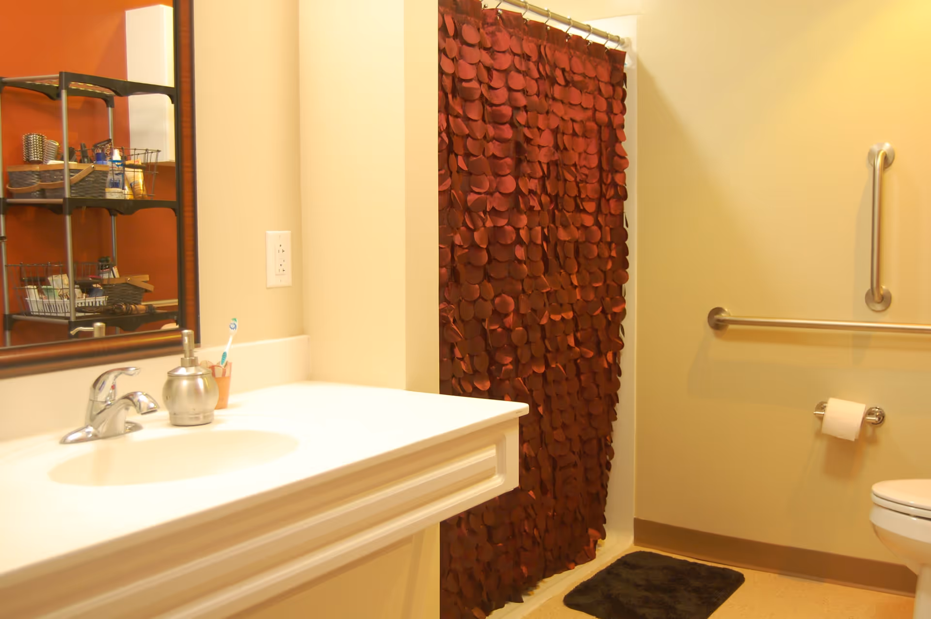 A bathroom featuring a white sink, a red shower curtain with petal designs, a mirror, and a shelf with toiletries.
