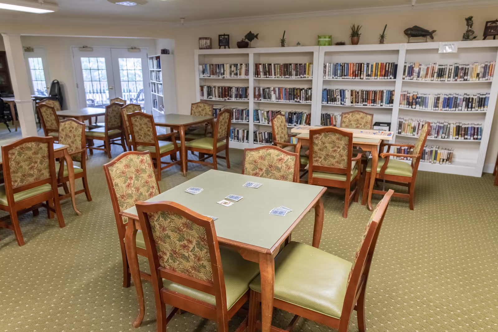 Community library/activity room with tables, chairs, and wall-to-wall bookshelves.