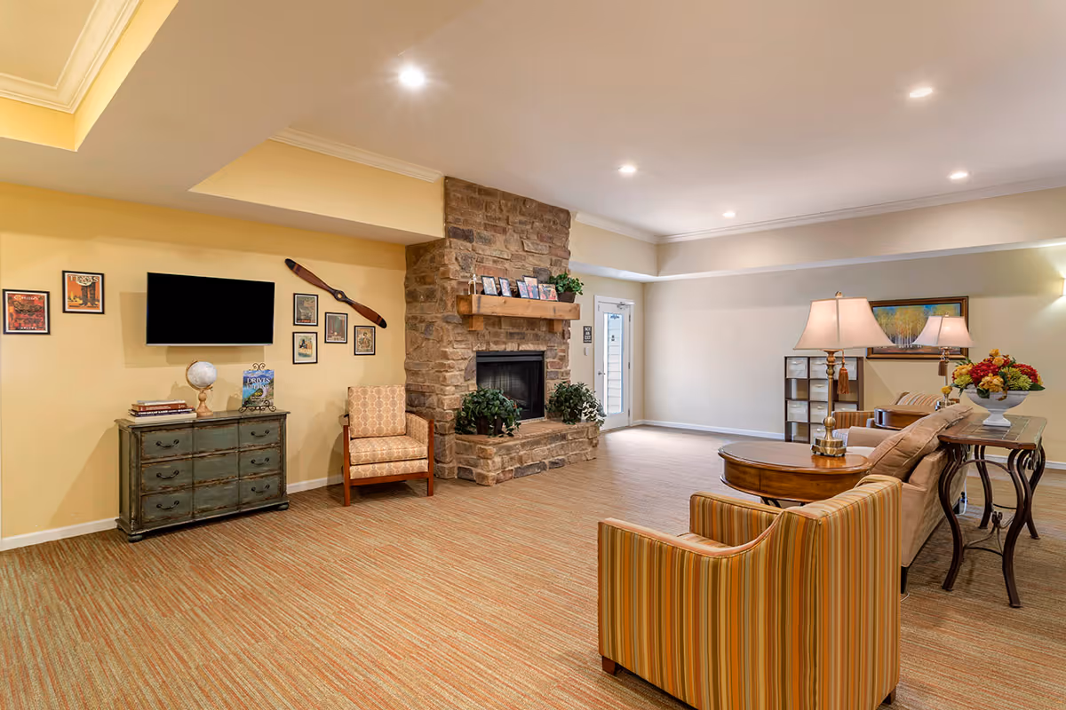 Bright common living room with a stone fireplace, wall-mounted TV, seating and lamps.