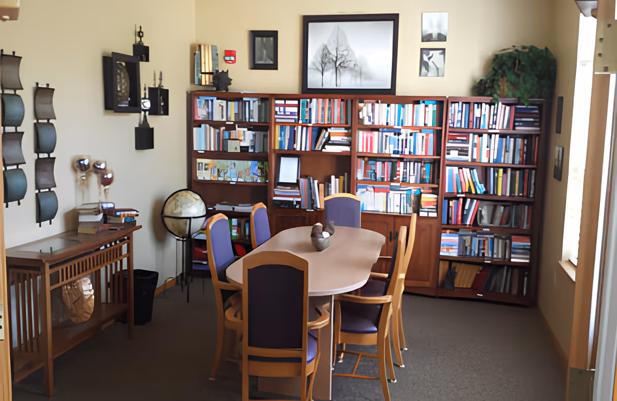 A small communal library/meeting room with a central table and chairs and bookshelves along the back wall.