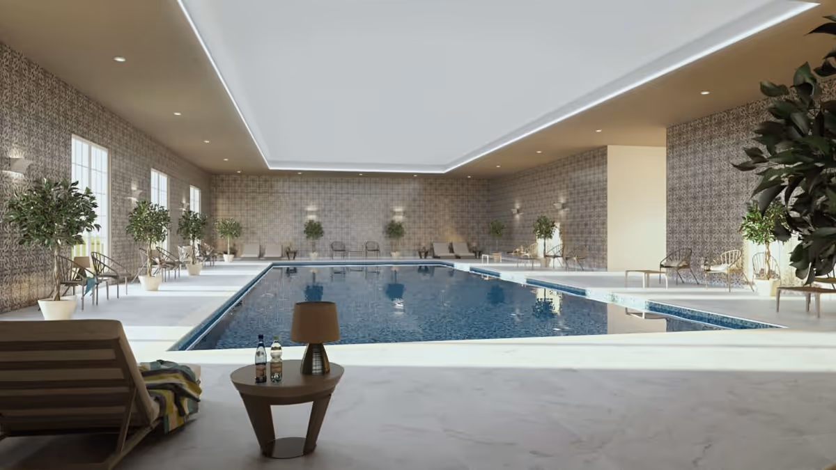 Indoor swimming pool area with lounge chairs, potted plants, and a small table with a lamp and two bottles on it. The pool is surrounded by patterned walls and large windows letting in natural light.