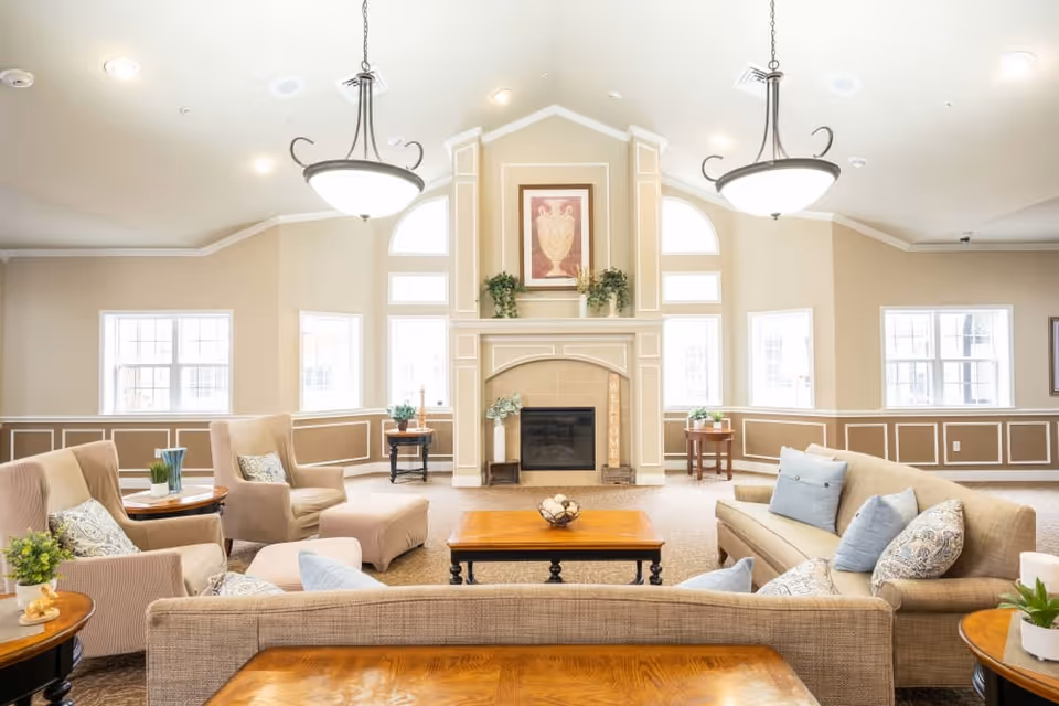 Bright, spacious common living room with sofas, armchairs, a central coffee table, and a fireplace beneath decorative artwork.