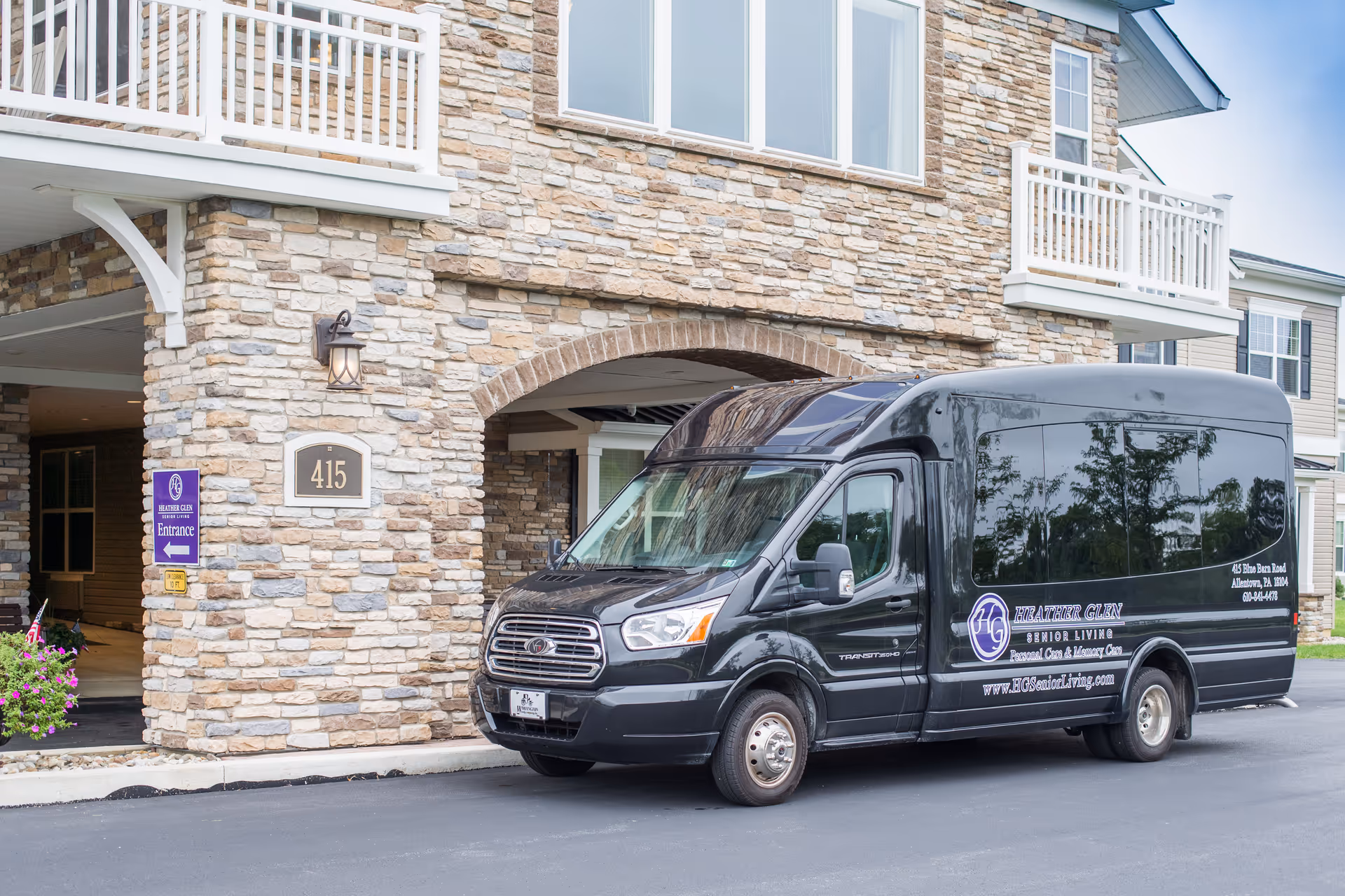 A black Heather Glen Senior Living shuttle van parked outside the stone-faced entrance of a senior living building marked 415.