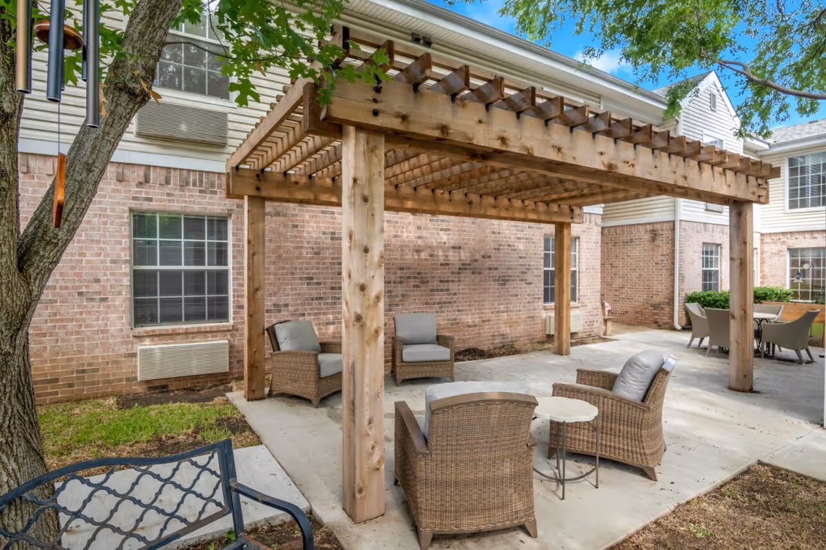 Outdoor courtyard with a wooden pergola, wicker seating and tables in front of a brick building.
