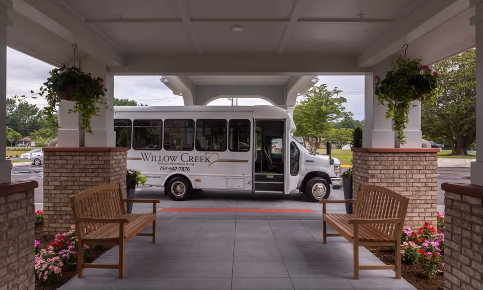 Covered entrance with wooden benches and a Willow Creek shuttle bus parked under the porte-cochere.