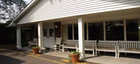 Front view of Brookdale Liverpool shows a covered entry with benches and potted plants.