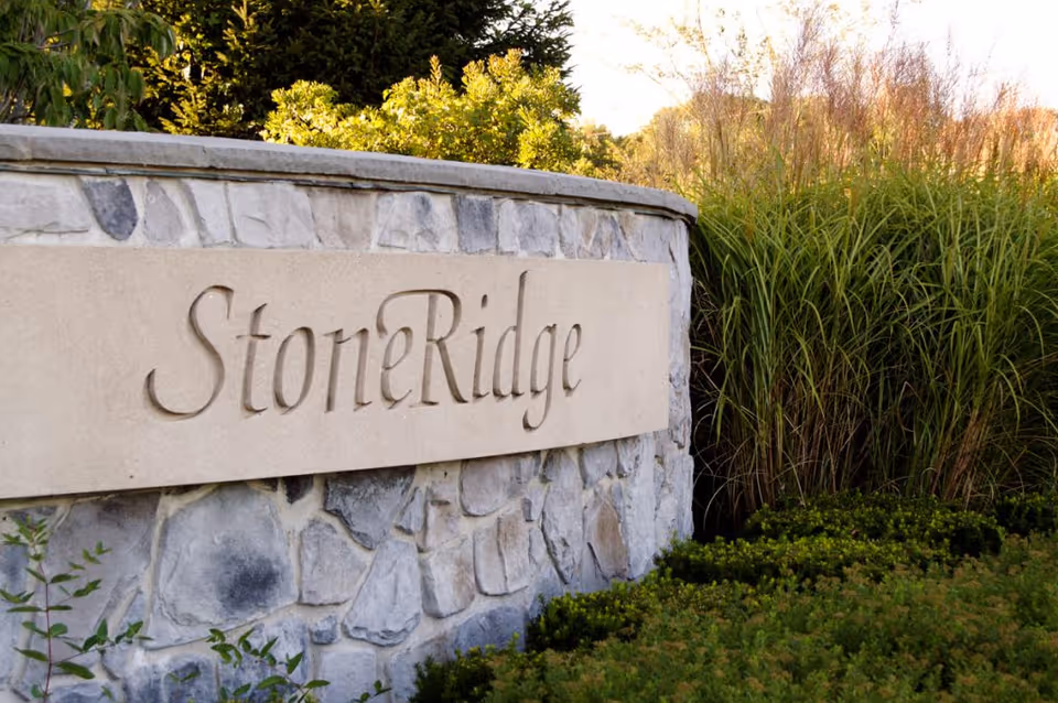 StoneRidge sign carved into a stone wall surrounded by green bushes and tall grass in an outdoor setting.