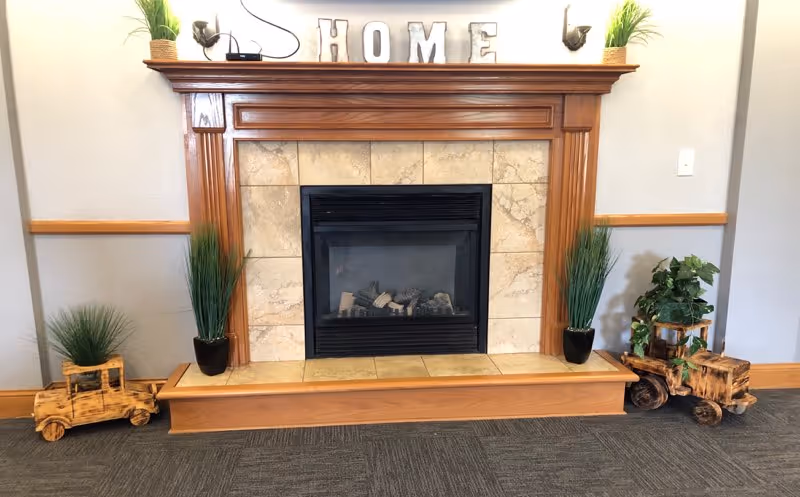A decorative gas fireplace with a wooden mantel, tile surround, potted plants, and letters spelling "HOME" on the mantel.
