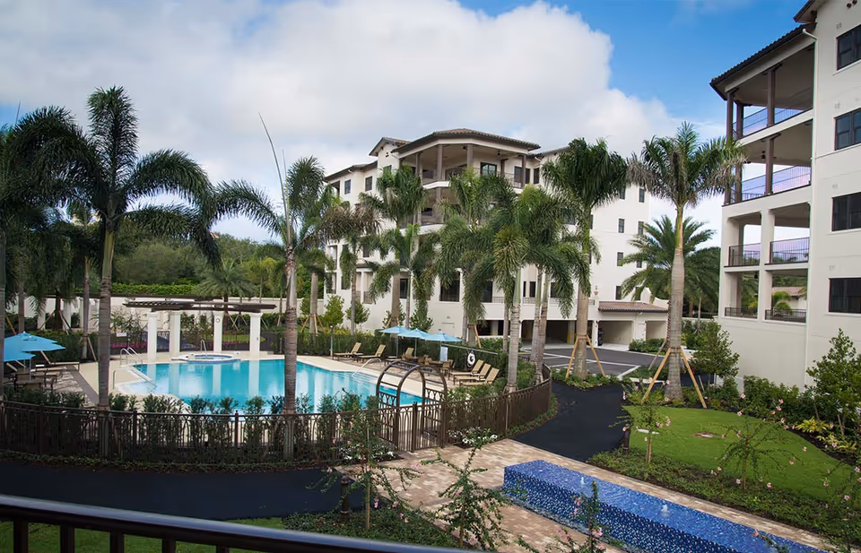 Resort-style courtyard with a swimming pool surrounded by palm trees and multi-story residential buildings.