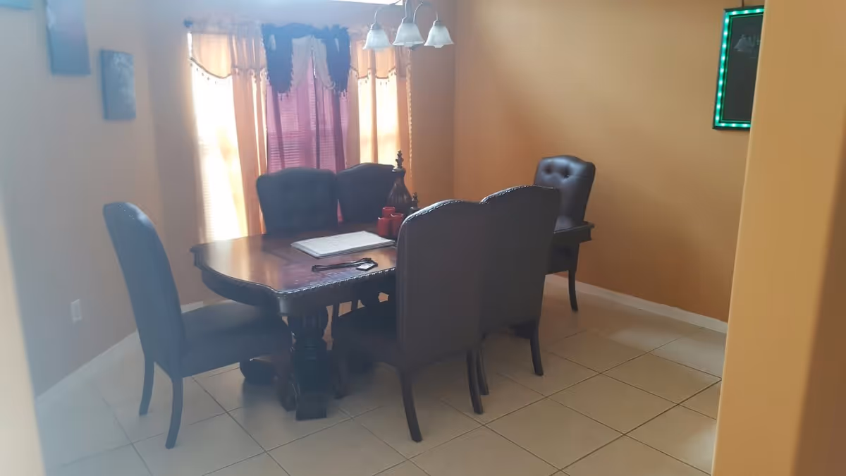 Dining room with a dark wood table and six upholstered chairs on a tiled floor, with a curtained window and warm-colored walls.