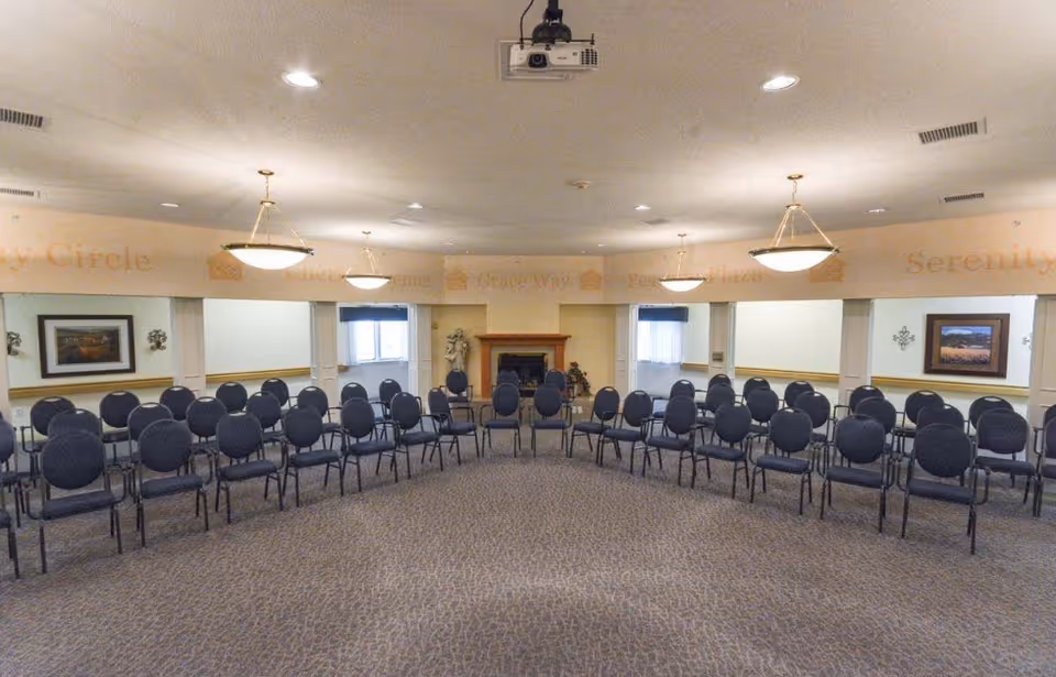 Large meeting/activity room with rows of chairs facing a fireplace and a ceiling-mounted projector.