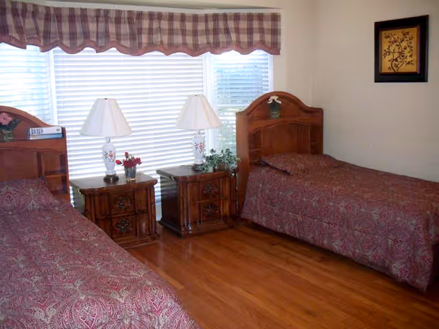 Two twin beds with matching wood headboards, nightstands, lamps, and window blinds in a shared bedroom.