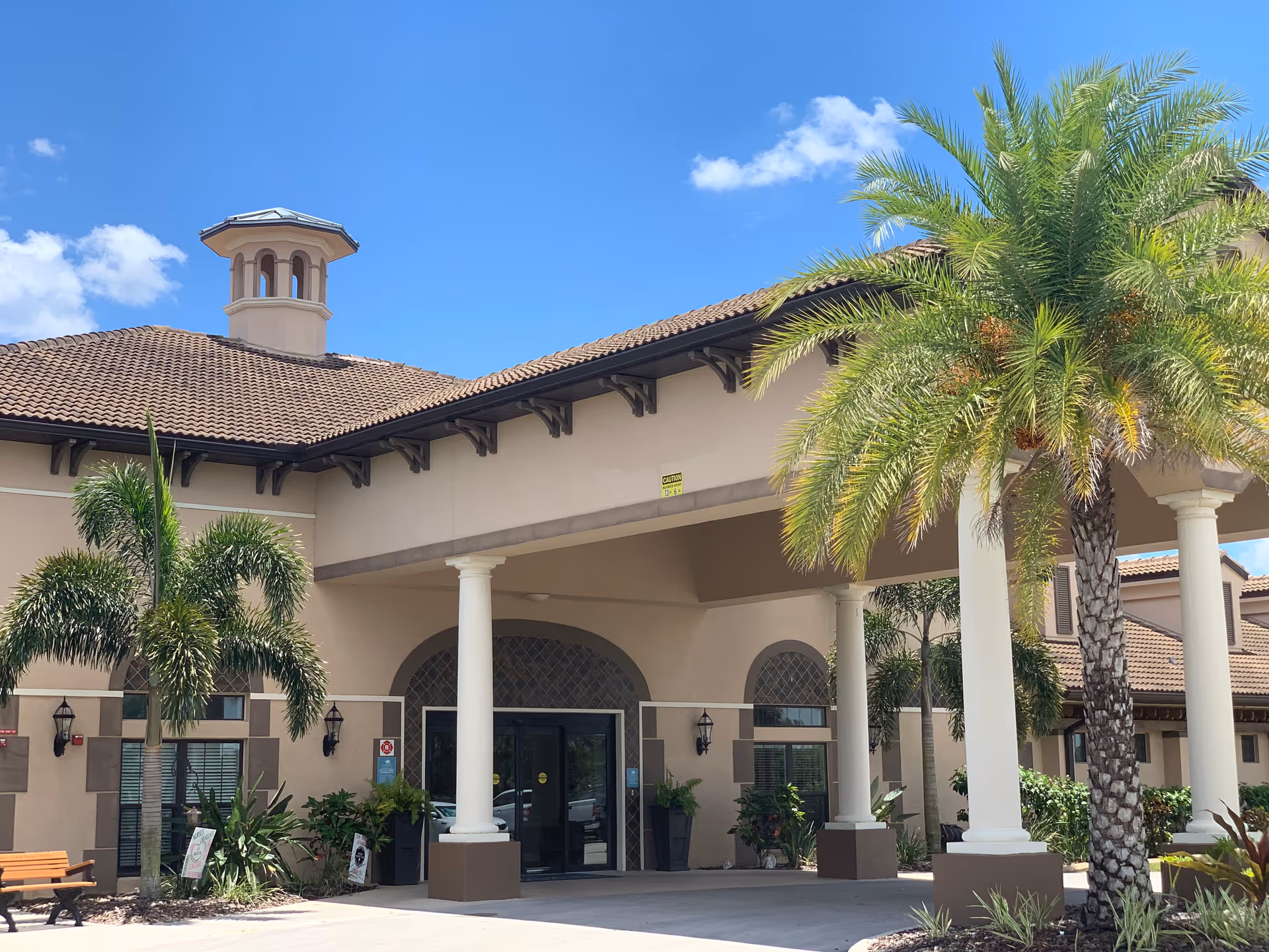 Front exterior of Palm Bay Memory Care with arches, columns, and palm trees.