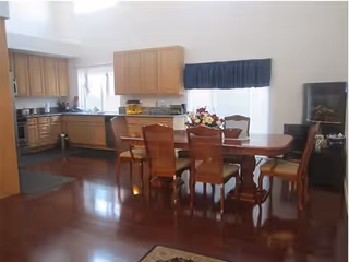 Open-plan interior showing a wooden dining table with chairs next to a kitchen with light wood cabinets and polished hardwood floors.