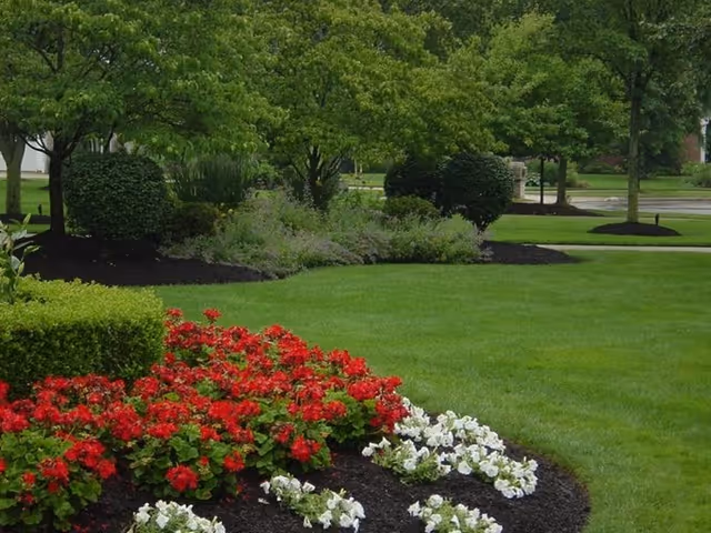 Well-maintained landscaped lawn with red and white flower beds, trimmed bushes, and trees.
