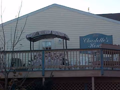 Exterior view of a senior living facility with a blue Charlotte's Home sign on a deck.