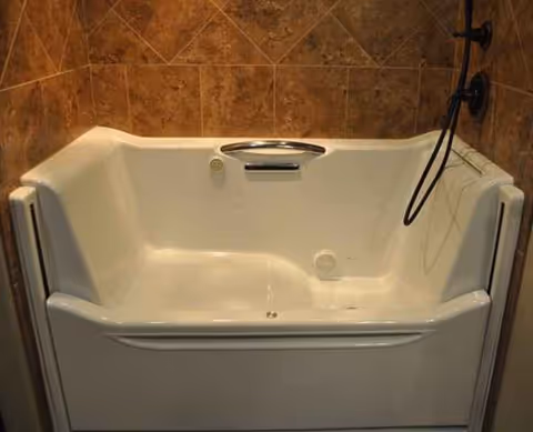 A white bathtub installed in a brown-tiled bathroom with a handheld shower.