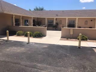 A single-story beige senior living facility with a covered front walkway and small landscaped planters along the entrance.