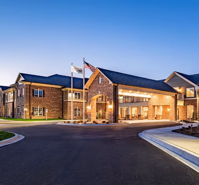 Exterior view of American House Mount Prospect, brick facility with flagpoles and lit entrance.