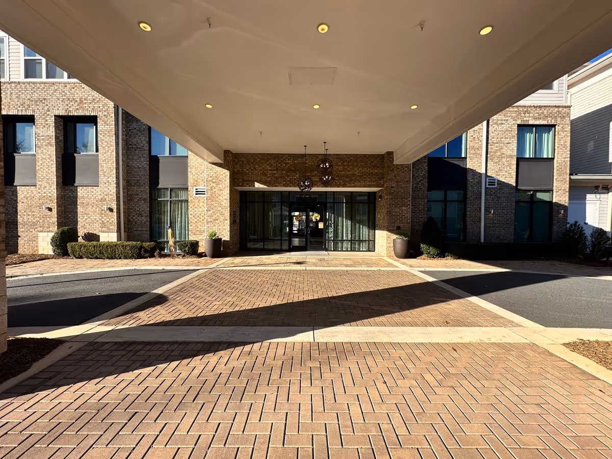 Covered driveway and main entrance of a brick senior living building with glass doors and potted plants.