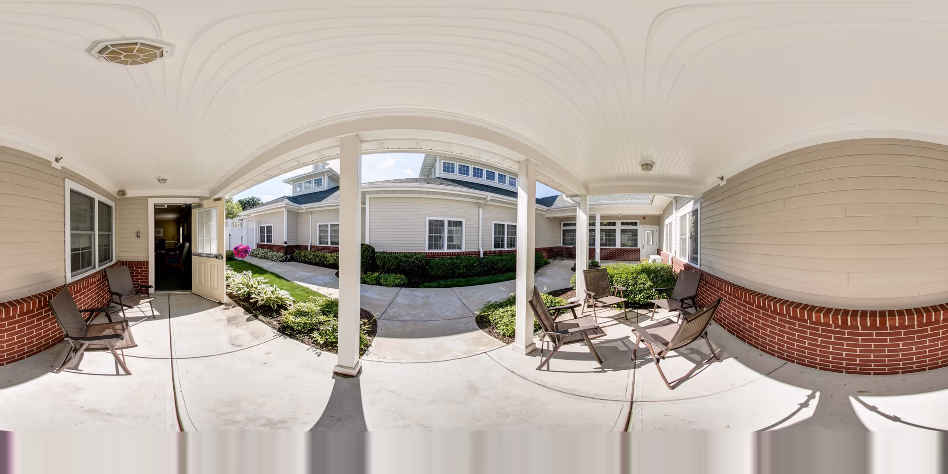 Covered courtyard walkway with chairs and entrances to a senior living building.