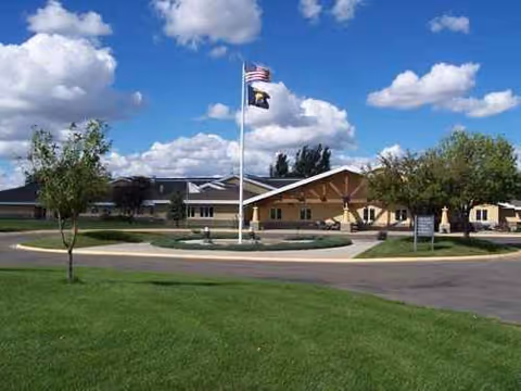 Exterior view of Eastern Montana Veterans Home with flagpoles, circular driveway, and green lawn.
