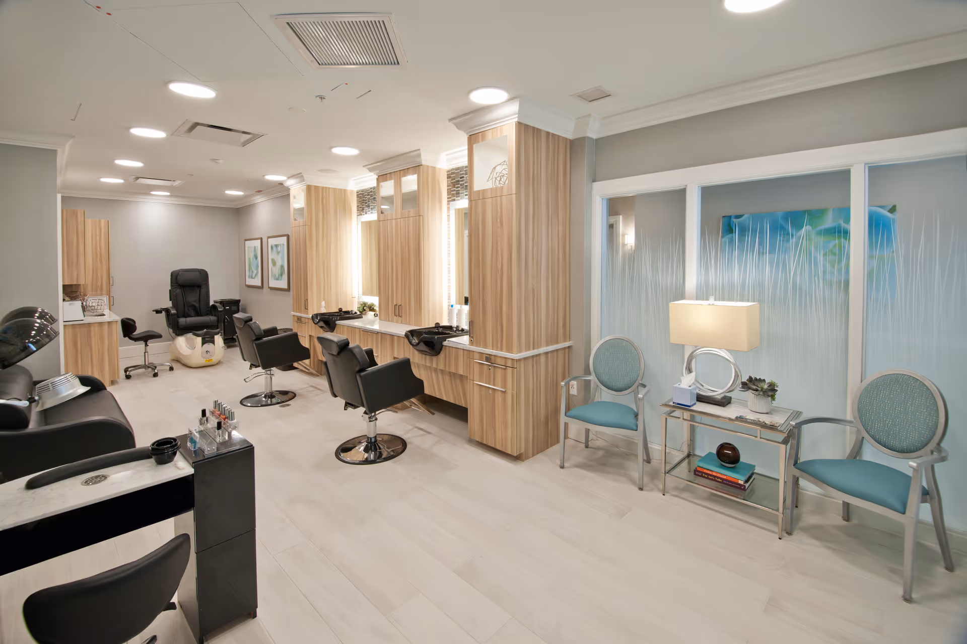 Bright, modern salon area with styling chairs, wash stations, mirrors, and a small seating table with chairs.
