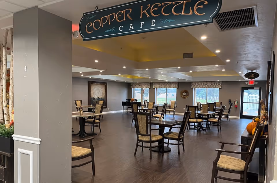 Spacious dining area with multiple tables and chairs beneath a hanging sign reading 'Copper Kettle Café'.