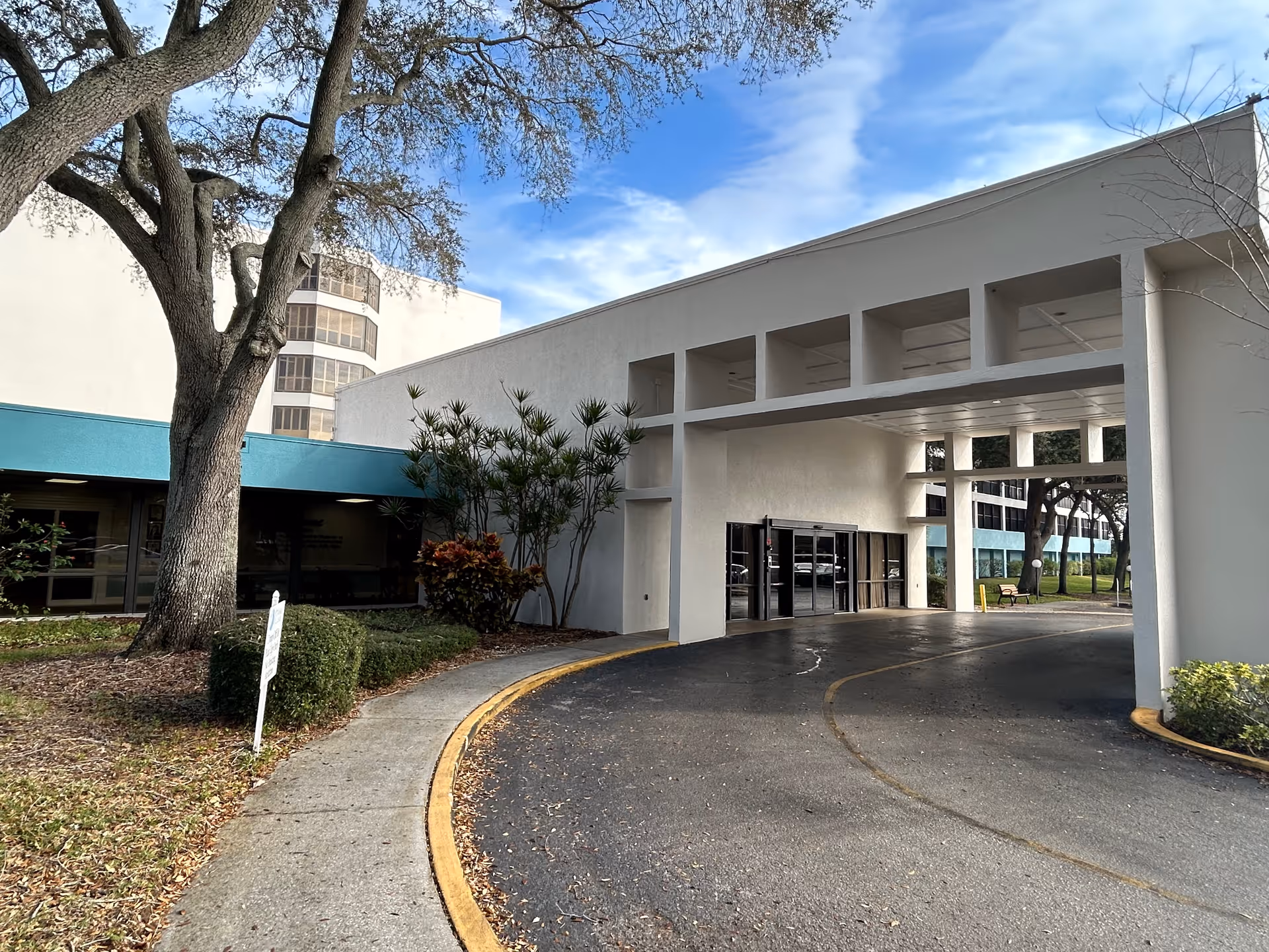 Covered drive-through entrance and facade of a senior living facility with a curved driveway and trees.