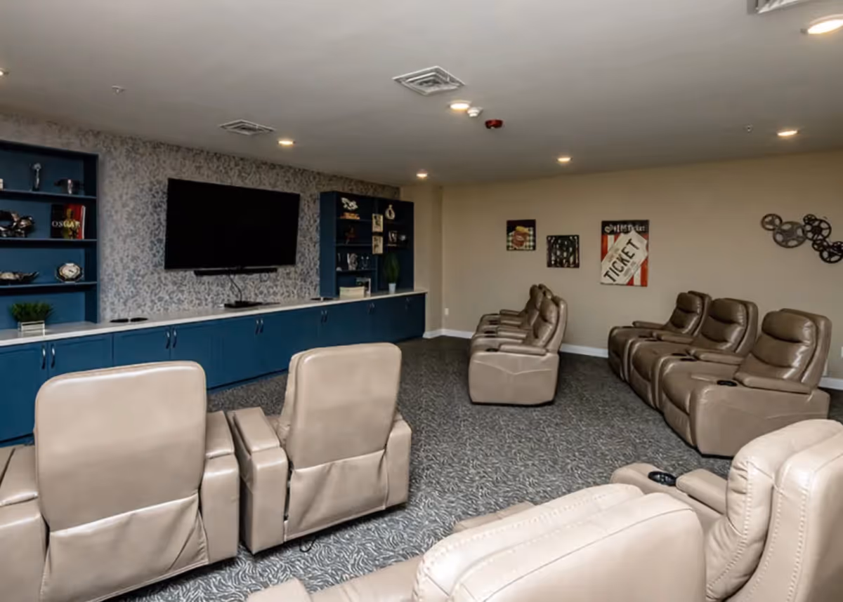 A media/lounge room with rows of beige recliner chairs facing a wall-mounted TV and blue built-in cabinets.