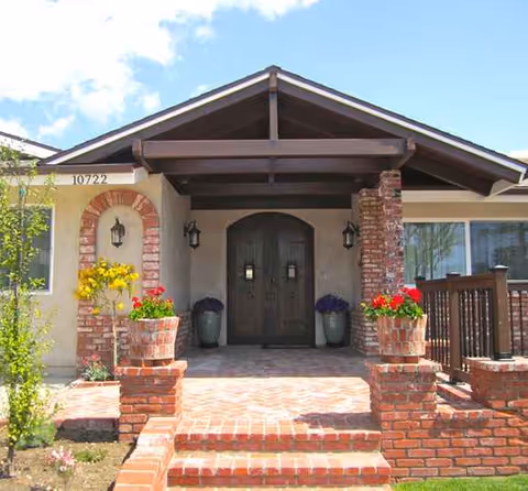 Brick front entrance with arched door, planters, and a shaded porch.