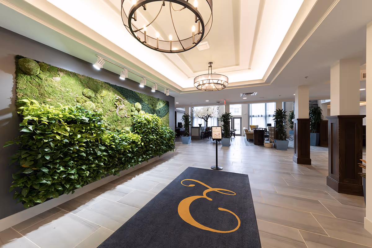 Spacious modern lobby with a living green wall, chandeliers, and a carpeted entrance mat bearing a stylized 'E'.