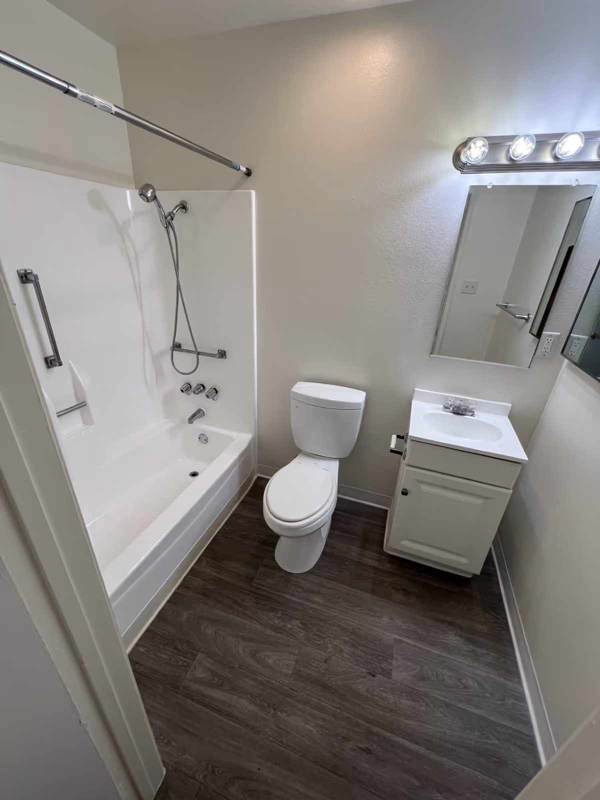 Small clean bathroom with a bathtub/shower combo, toilet, and single-sink vanity beneath a mirror and light fixture.