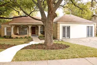 Single-story senior living house with a front porch, driveway, and large tree.