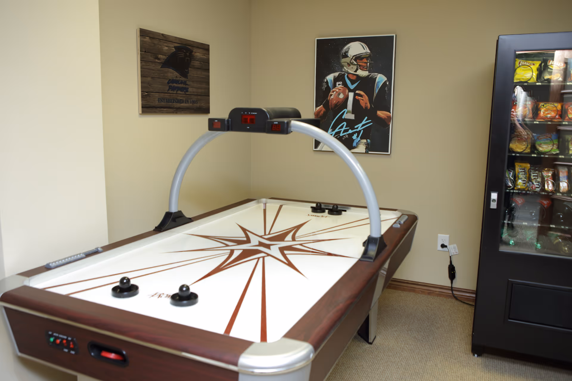 Air hockey table in a small game room with a vending machine and sports posters on the wall.