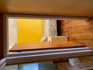 View through an open doorway into a room with wooden flooring, a yellow wall, a patterned sofa, and a small white cabinet.