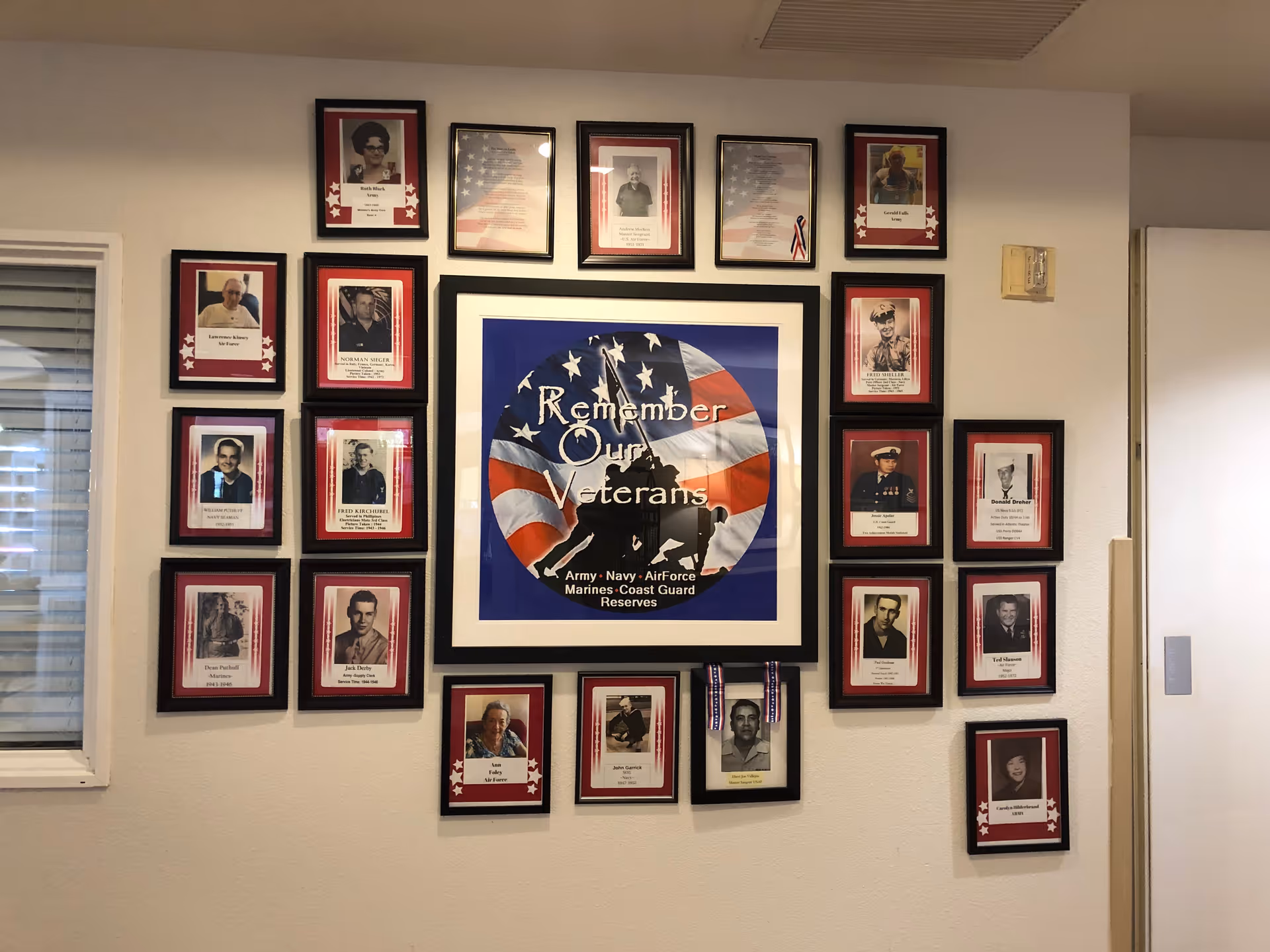 Interior wall display of framed veteran portraits surrounding a central 'Remember Our Veterans' poster.