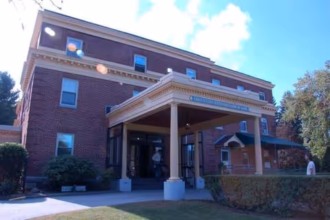 Brick senior living facility with columned entrance; a few people near the doorway.