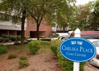 Exterior view of Chelsea Place Care Center with blue sign, trees, and parked cars.