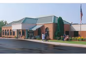 Brick facility exterior with entrance, flagpole, and a few people near the doorway.