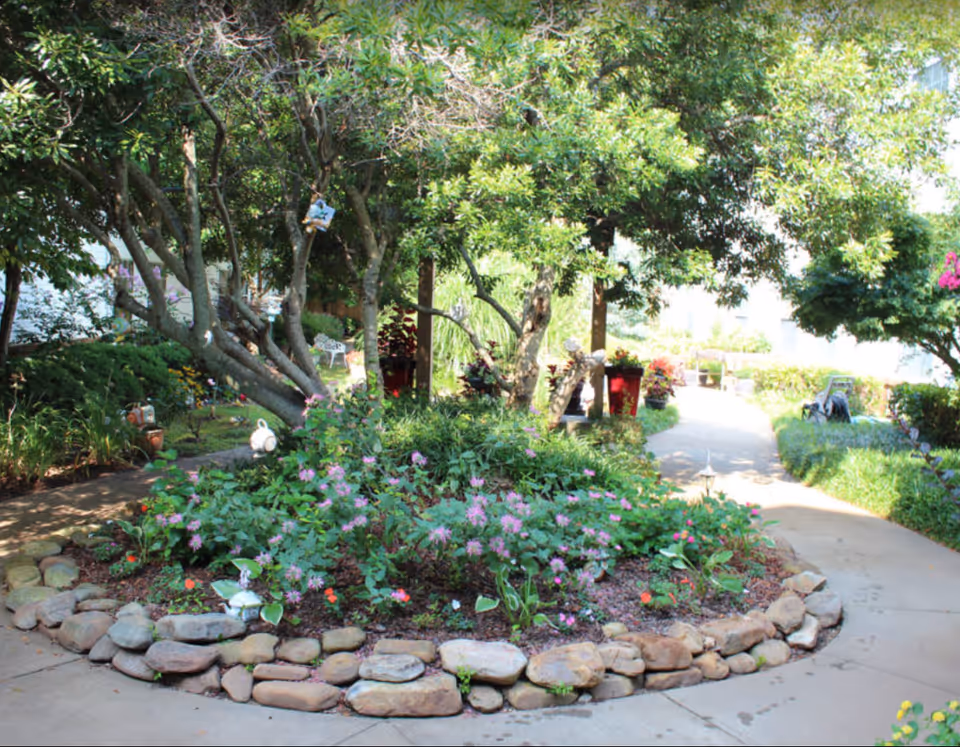 Shaded courtyard with a circular rock-bordered flower bed, trees, and walkways.