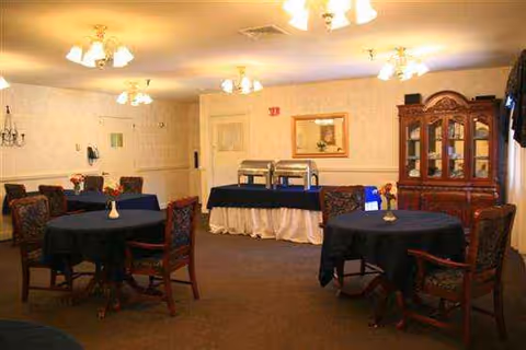 An interior dining room with round tables, chairs, chandeliers, and a buffet along the back wall.