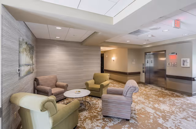 Small seating area with upholstered armchairs around a round table and an elevator visible in the background.